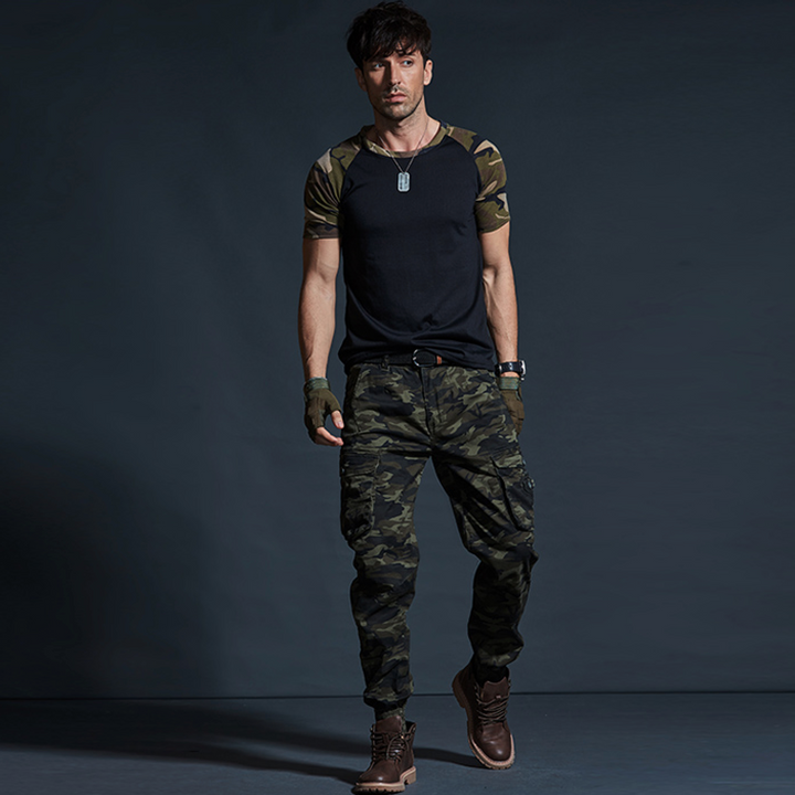 Un homme porte un pantalon cargo kaki camo avec des chevilles resserrées. Le pantalon est de coupe droite et comporte des poches cargo latérales. Fabriqué en coton de haute qualité, il allie fonctionnalité et style militaire. Disponible dans les tailles 28 à 40.