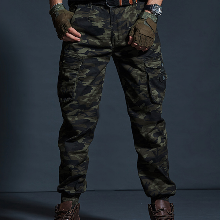 Un homme portant un pantalon cargo kaki camo avec des poches cargo latérales et des chevilles resserrées.