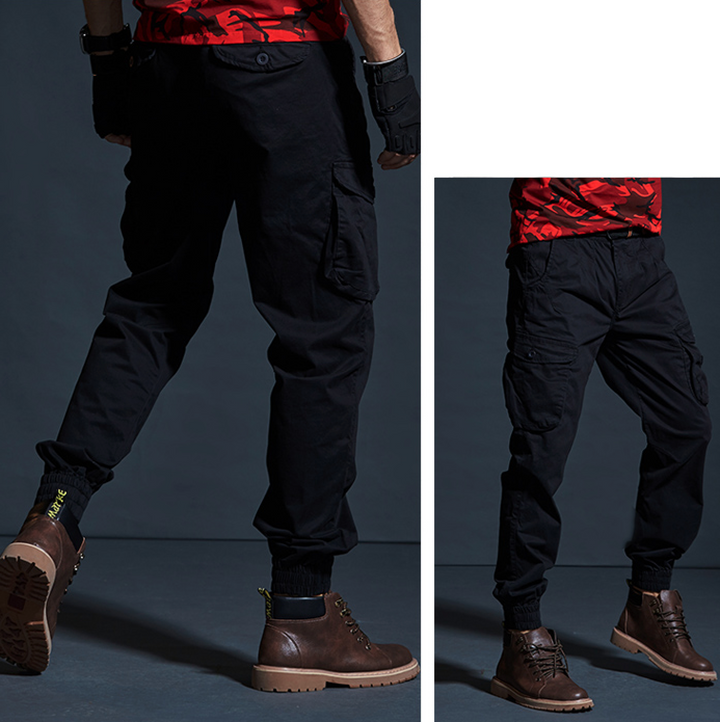 Un homme portant un pantalon cargo en coton noir avec des chevilles resserrées. Style militaire avec poches cargo latérales. Disponible du 28 au 40. Confortable et durable.