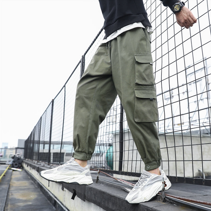 Un homme debout sur une planche à roulettes, portant un pantalon cargo ample multipoches resserré aux chevilles kaki - Homme.