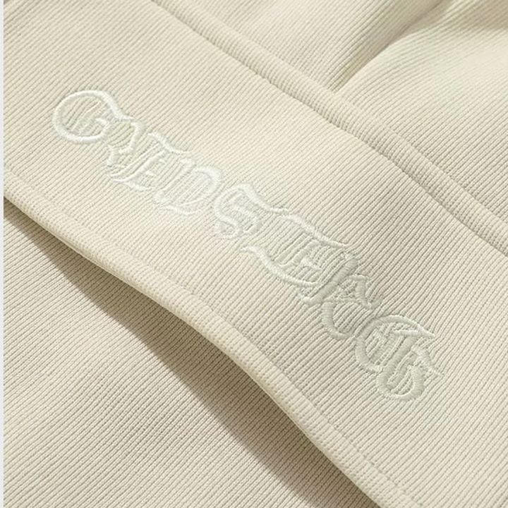 Un gros plan sur un pantalon cargo baggy blanc crème pour homme. Tissu épais et résistant en polyester pour une durabilité optimale. Tailles disponibles du S au 2XL. Inscription cousue sur une poche latérale pour une touche streetwear. Liberté de mouvement optimale grâce à l'ampleur du pantalon.