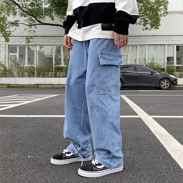 Un homme pose dans la rue en pull noir et blanc, baskets blanches et noires et pantalon baggy avec lien à la cheville bleu clair.