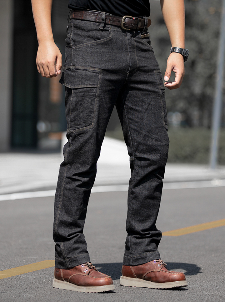 Un homme debout sur une route, portant un jean cargo ajusté coupe droite noir. Le jean est doté de nombreuses poches et d'une couture camo kaki discrète sur l'une des poches à la taille. Fabriqué en toile denim stretch pour un confort optimal et une grande liberté de mouvement. Disponible du S au 2XL.