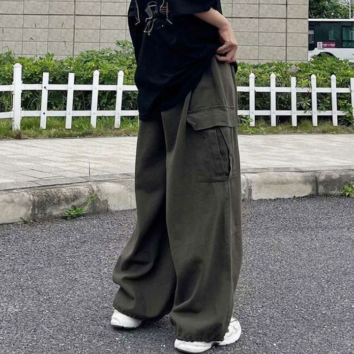 Une personne debout à l'extérieur, les mains sur les hanches, portant le Pantalon cargo baggy extra-large kaki pour femme de Cargo District. Coupe baggy extra-large pour un confort inégalé et une allure street. Taille haute avec élastique pour un ajustement parfait. Élastique aux chevilles pour une esthétique tendance. Tailles disponibles du M au 3XL.