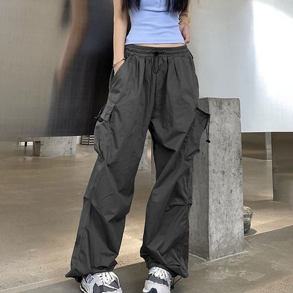 Une femme porte un crop top bleu, des baskets et un pantalon cargo baggy léger gris. Elle pose dans la rue.