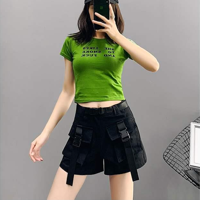 Une femme prend un selfie avec un short cargo noir à ceinture lanières à clip. Le short est ample et taille haute, offrant confort et style urbain. Les poches cargo sont ornées de lanières à clip, ajoutant une touche tendance. Disponible du S au 2XL. (Cargo District - Vente de vêtements de style cargo)