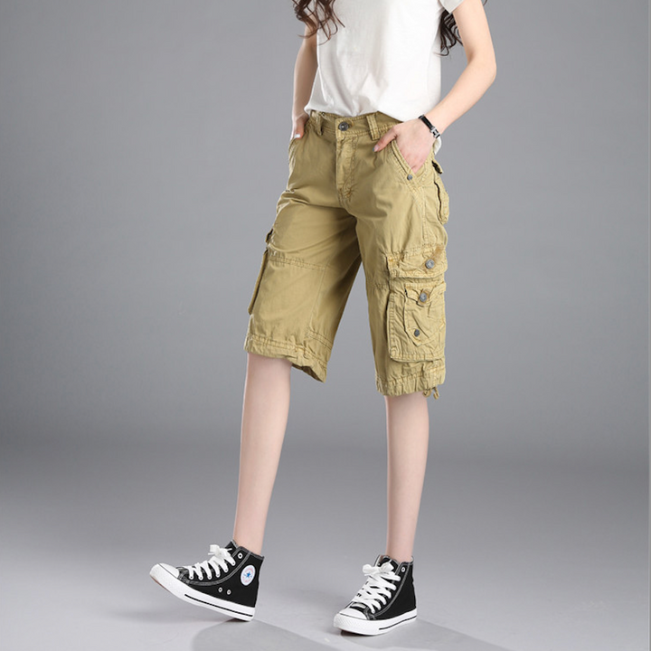 Une femme portant un short cargo long coupe droite beige avec des poches cargo latérales. Un look urbain simple et audacieux pour un style décontracté. Disponible en tailles US 28 à 38. Fabriqué en coton pour un confort maximal et une excellente durabilité.