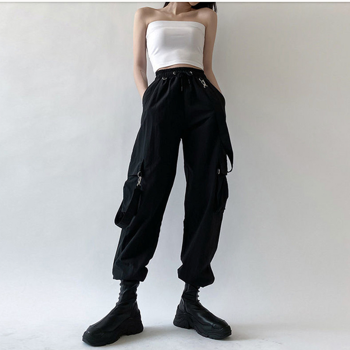 Femme portant un pantalon cargo noir avec sangles bretelles amovibles. Coupe droite, taille haute et élastique pour un ajustement confortable. Disponible du S au 3XL.