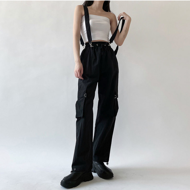 Une femme porte un pantalon cargo noir avec des sangles bretelles amovibles. Ce pantalon cargo taille haute en coton offre un ajustement confortable et sûr. Disponible du S au 3XL, il ajoute une note d'originalité à votre style urbain et street.