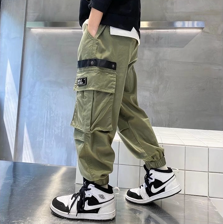 Un garçon porte un pantalon cargo jogger large kaki avec des poches latérales pratiques et une taille élastique.