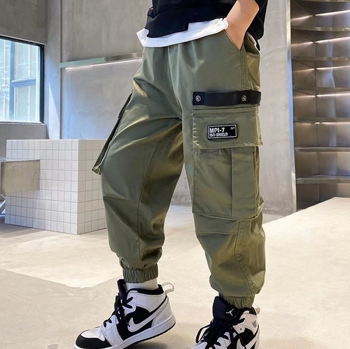 Un garçon porte un pantalon cargo jogger large de couleur kaki avec des poches latérales pratiques et une taille élastique.