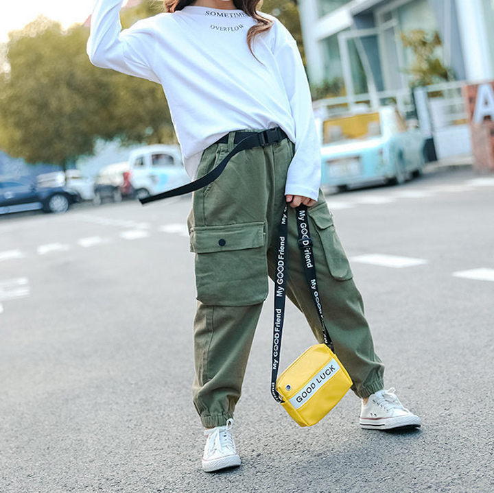 Une femme portant un pantalon cargo jogger kaki avec ceinture clip. Le pantalon affiche un style urbain et tendance avec des poches latérales et une ceinture noire à clip. Disponible du 5 au 14 ans.