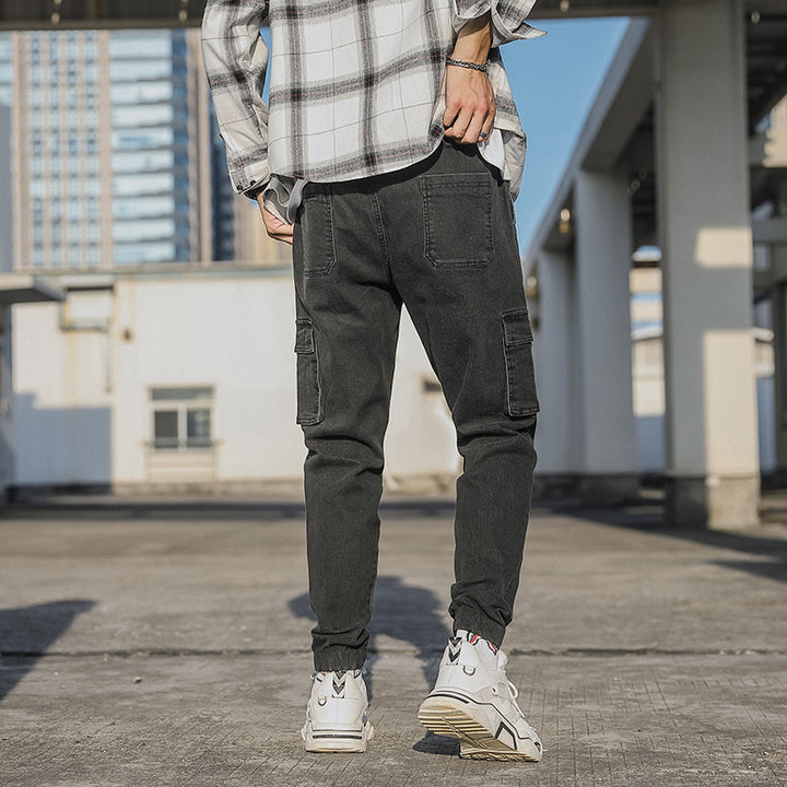 Un homme debout sur un toit, portant un jean cargo noir aux chevilles resserrées. Coupe droite pour homme, avec poches latérales et élastique à la taille et aux chevilles. Disponible du XS au 5XL.