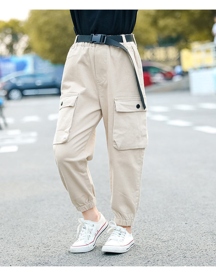 Une personne portant un pantalon cargo jogger beige avec ceinture clip, faisant partie de la collection pour fille de Cargo District. Le pantalon affiche un style urbain et tendance avec des poches latérales et une ceinture noire à clip. Disponible en tailles de 5 à 14 ans.