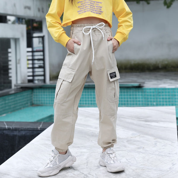 Une fille pose à l'extérieur avec un pull jaune et un pantalon cargo taille haute beige. Le pantalon taille haute avec élastique et cordon  est resserré aux chevilles.