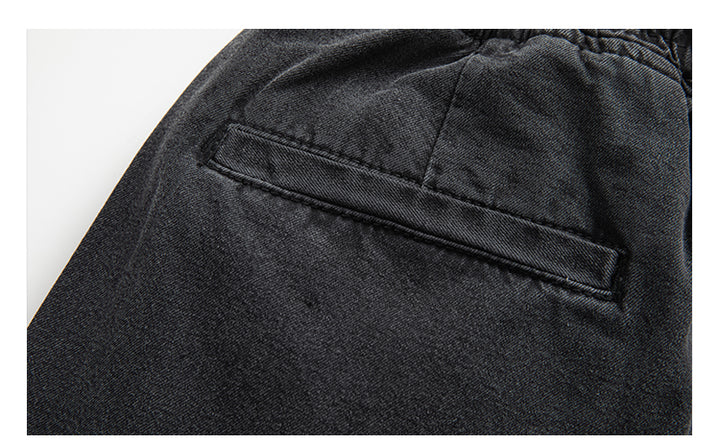 Un gros plan sur un pantalon noir cargo jogger coupe large pour homme. Confortable et tendance, ce pantalon en toile denim garantit durabilité et style décontracté. Tailles disponibles du S au 2XL. Poches latérales inclinées fermées par des boutons ajoutant une touche unique.