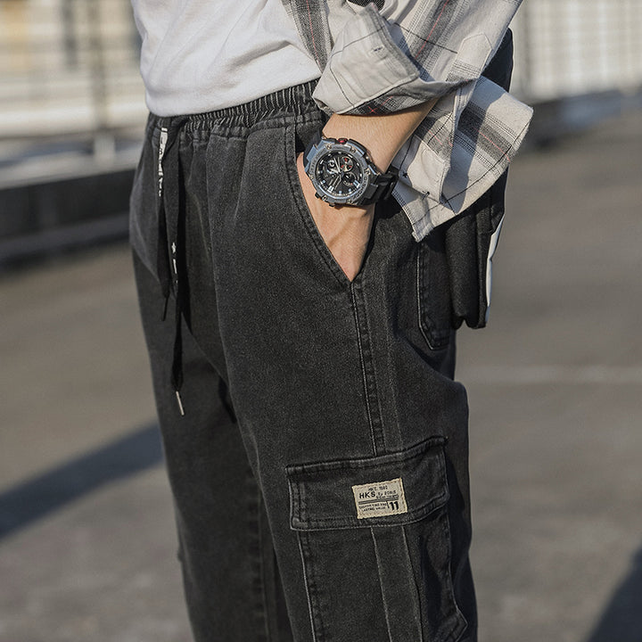 Un homme portant un jean cargo noir avec les mains dans les poches et une montre au poignet.