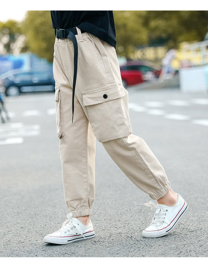 Un enfant porte un pantalon cargo jogger beige avec ceinture clip, faisant partie de la collection Cargo District pour fille. Le pantalon a des poches latérales et un style urbain et tendance. Tailles disponibles du 5 au 14 ans.