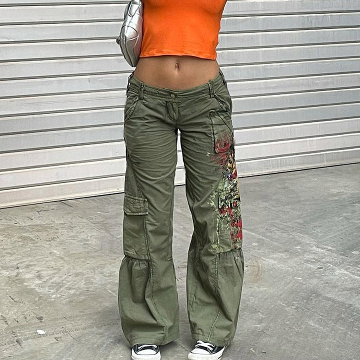 Une femme portant un pantalon cargo kaki à motif, taille basse. Un ajout audacieux à votre style urbain avec sa coupe flatteuse et ses poches cargo pratiques. Disponible du S au L.