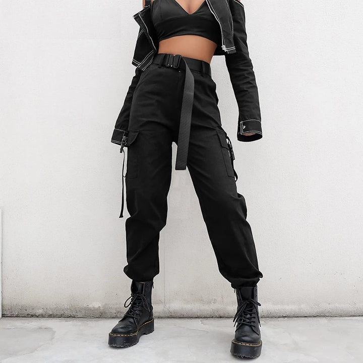 Une femme porte un pantalon cargo noir avec des poches à clips aux chevilles. Le pantalon est conçu en coton pour un confort maximum et une tenue durable. Disponible du S au 3XL, il met en valeur la silhouette avec sa coupe droite et sa taille haute. Parfait pour un look urbain audacieux.