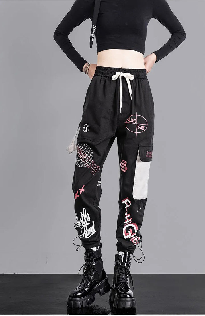 Une femme portant un pantalon noir avec des patchs, des bottes noires et un logo. Pantalon cargo jogger à motif - Noir - Femme.