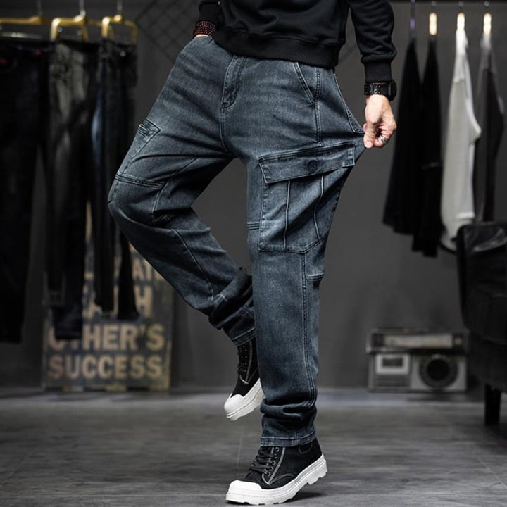 Un homme portant un jean cargo bleu coupe droite avec poches latérales à pression. Matière denim extensible pour un confort optimal. Disponible du 28 au 44.