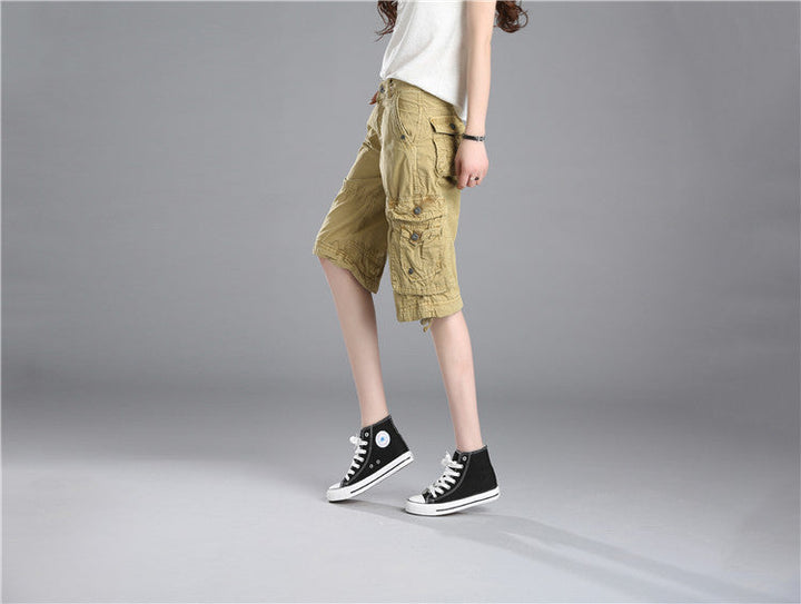 Une personne porte des baskets noires et blanches avec un short cargo long coupe droite beige. Le short a une coupe ample et des poches cargo latérales pour un look décontracté. Disponible en tailles US 28 à 38. Image du produit du magasin Cargo District.