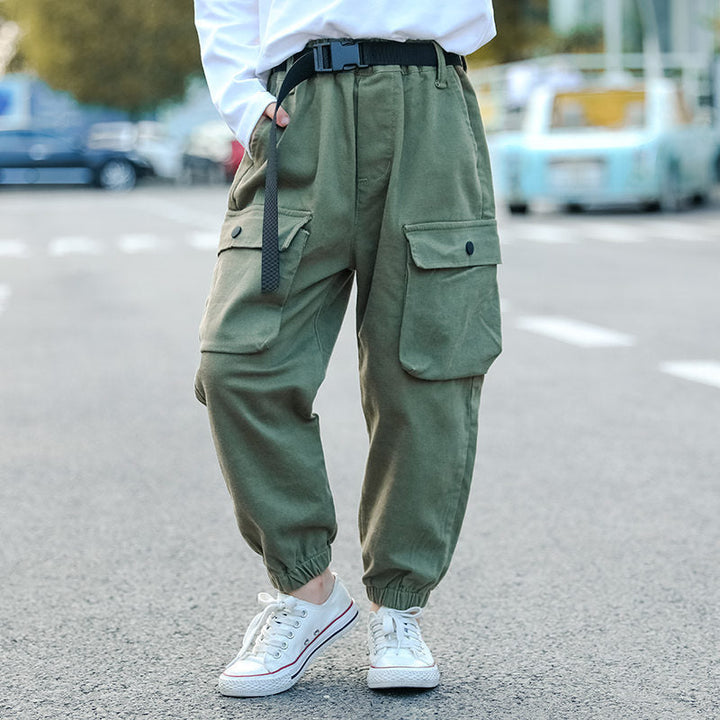 Une fille pose dans la rue. Elle porte un haut noir, des baskets basses blanches et un pantalon cargo jogger kaki avec ceinture à clip noire.