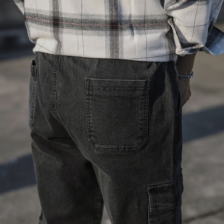 Un homme portant un jean cargo noir avec des poches latérales et une coupe droite resserrée aux chevilles. Disponible dans différentes tailles.