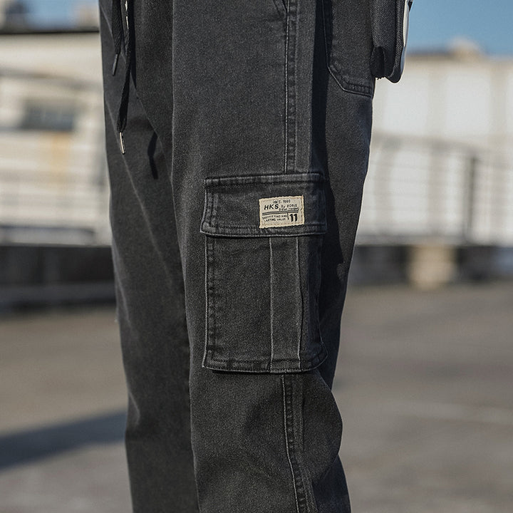 Un homme portant un jean cargo noir coupe droite resserré aux chevilles, avec des poches latérales et un ajustement parfait grâce à l'élastique à la taille et aux chevilles. Disponible dans différentes tailles.