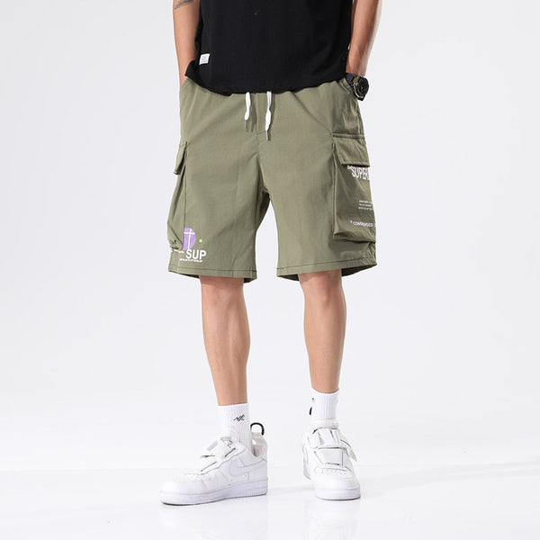 Un homme porte un short cargo kaki ample avec inscriptions. Il porte des baskets montantes blanches et un tee-shirt noir.