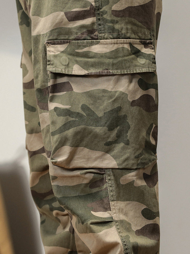 Un pantalon cargo kaki coupe large resserré aux chevilles pour homme avec motif camouflage militaire. 100% coton pour un confort et une durabilité optimale. Tailles US 28 à 38.