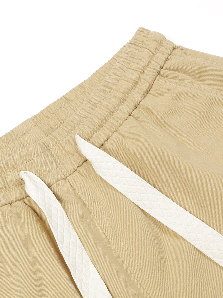 Un gros plan d'un short cargo en coton beige pour homme. Coupe baggy avec élastique à la taille et cordon de serrage pour un ajustement optimal. Élastique aux chevilles pour un look personnalisé. Disponible du S au 2XL.