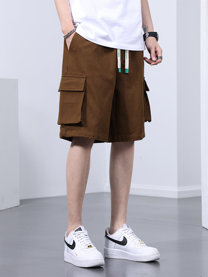 Un homme porte un short cargo marron, coupe large, avec des baskets blanches. Le short offre un confort optimal et une grande liberté de mouvement grâce à sa longueur jusqu'aux genoux et sa coupe ample. Disponible du M au 8XL.