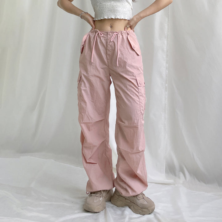 Une femme portant un pantalon rose taille basse, style cargo, avec une jambe large et élastique aux chevilles. Disponible du S au L. Confortable et urbain.