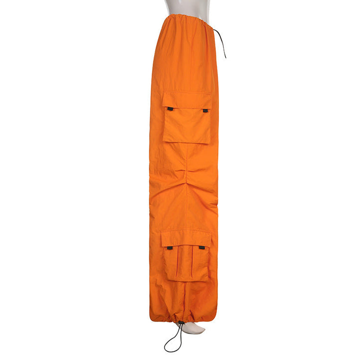 Un mannequin porte une combinaison orange ample de style cargo baggy pour femme, avec des lanières pendantes. Disponible en tailles S à L, cette tenue offre un confort sans égal et souligne la silhouette. Les chevilles élastiques ajoutent à l'effet baggy, tandis que la couleur rose apporte une touche de fraîcheur.