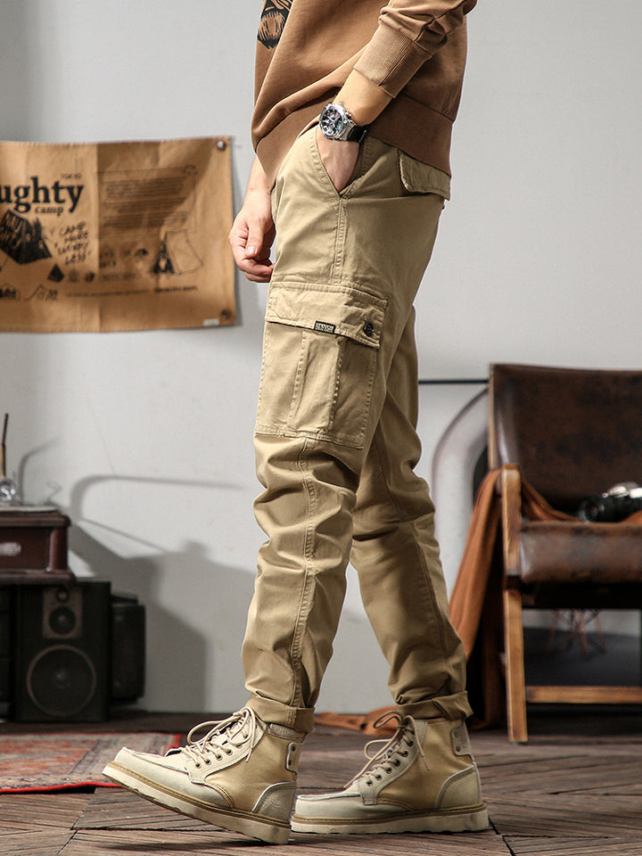 Un homme debout sur un skateboard, portant un pantalon cargo beige avec des poches cargo sur les côtés. Un choix intemporel pour un look masculin.