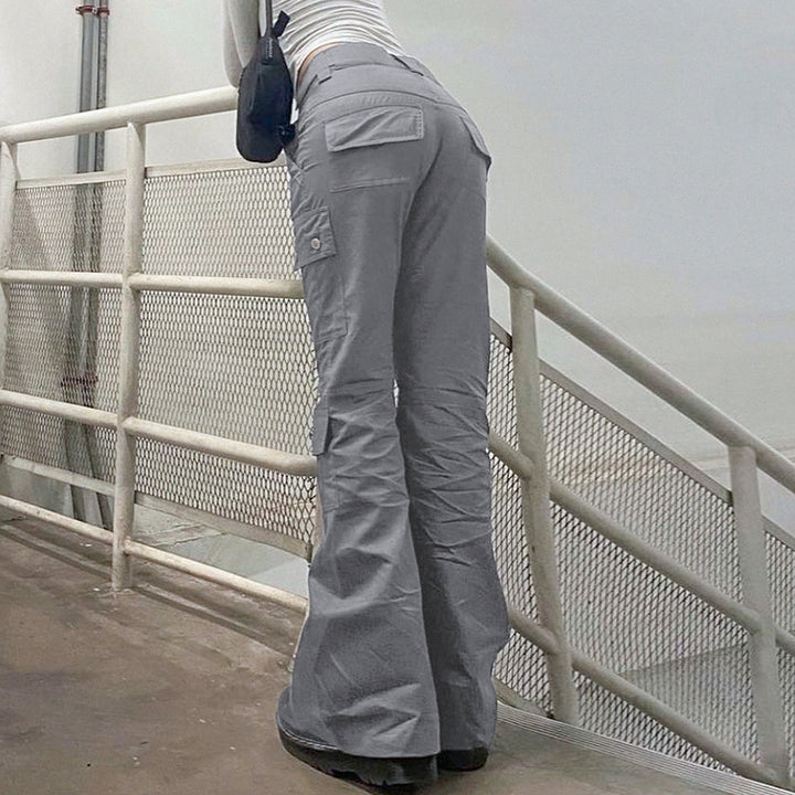 Une femme debout sur un escalier, portant un Pantalon cargo ajusté flare gris. Ce pantalon cargo taille haute met en valeur votre silhouette et vos courbes. Les poches utilitaires ajoutent une touche street à votre look. La coupe évasée au bas du pantalon apporte une note féminine et tendance. Disponible du S au L.