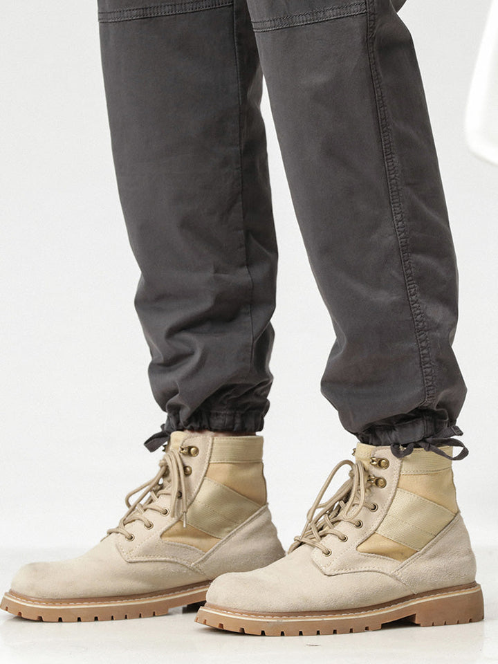 Un homme porte un pantalon cargo ample coupe droite gris avec des bottes blanches. Le pantalon est pratique avec des poches sur les côtés et une fermeture par bouton et fermeture éclair. Les bottes ajoutent une touche de style.