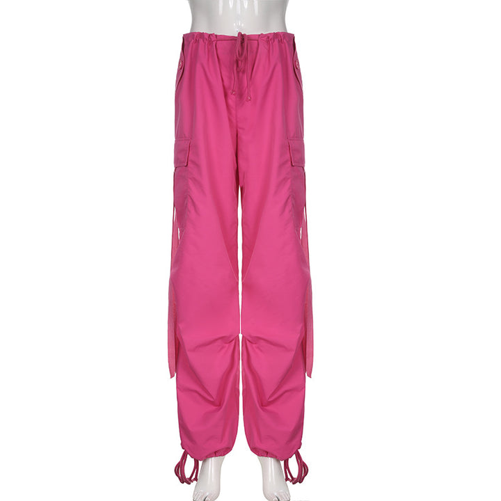 Un mannequin porte un pantalon cargo baggy taille basse rose pour femme, avec une coupe large façon parachute et des lanières pendantes. Confortable et extensible, ce pantalon est disponible du S au L. Les chevilles élastiques ajoutent à l'effet baggy. Le Pantalon cargo baggy taille basse - Rose - Femme de Cargo District.