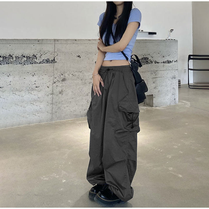 Une femme portant un Pantalon cargo baggy léger gris, avec une coupe baggy et des élastiques à la taille et aux chevilles pour un confort exceptionnel. Les poches latérales ajoutent une touche street et féminine. Disponible du S au 3XL.