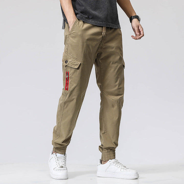 Un homme portant un pantalon cargo vert olive avec une fermeture rouge et des sneakers blancs.