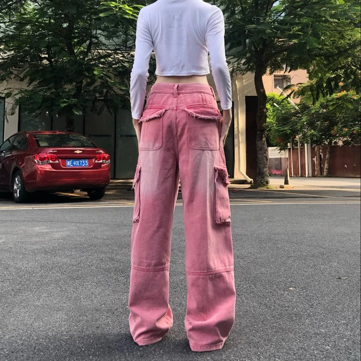 Une femme portant un jean cargo baggy rose délavé avec des déchirures judicieusement placées. Taille haute pour une silhouette moderne. Un look audacieux des années 2000 pour celles qui osent défier les conventions avec style. Disponible en tailles XS à XL.