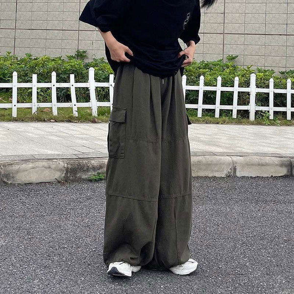 Une femme pose dans la rue avec un tee-shirt noir, des baskets blanches et un pantalon cargo baggy extra-large beige.