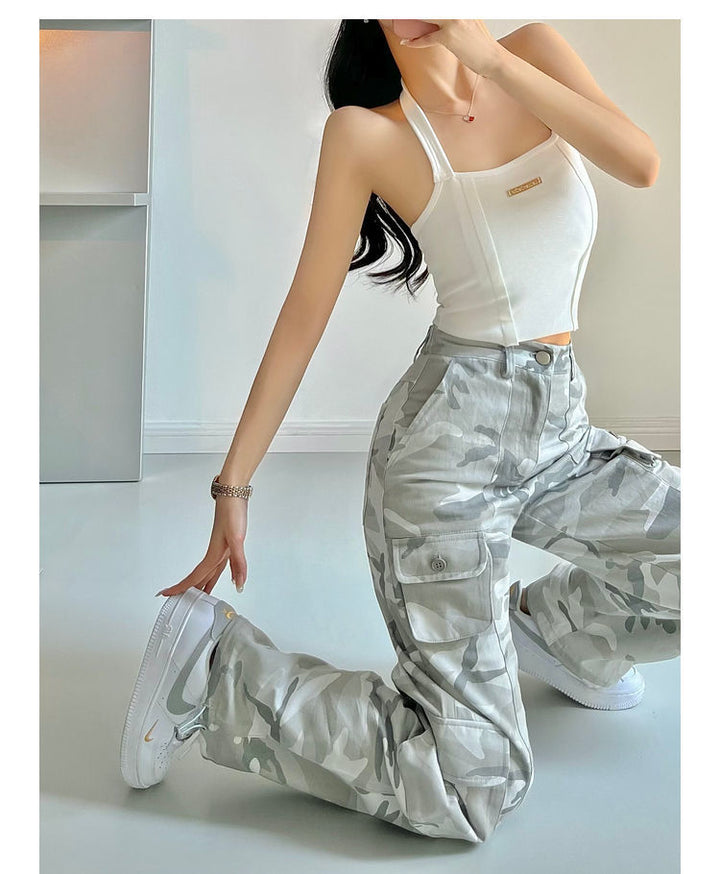 Une femme portant un pantalon cargo taille haute avec des jambes larges, motif gris camo. Le pantalon offre confort et style avec ses poches pratiques et sa taille élastique au dos. Disponible du M au 3XL.