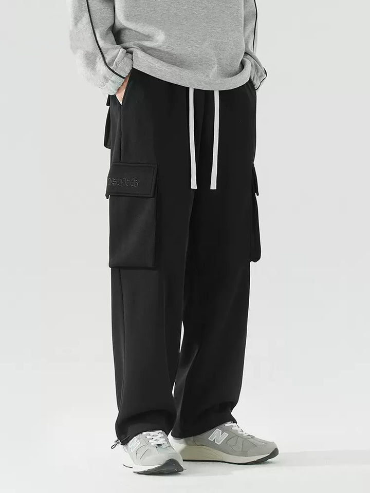 Un homme porte un pantalon cargo baggy noir, pull gris et baskets grises