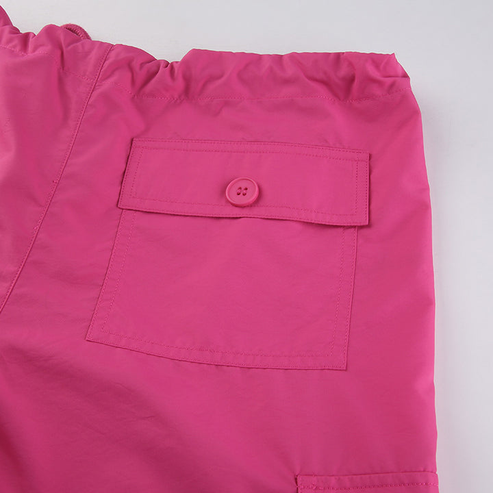 Un pantalon cargo baggy taille basse rose pour femme avec une coupe large façon parachute et des lanières pendantes. Confortable et extensible grâce à un mélange de polyester, jersey et spandex. Disponible du S au L.