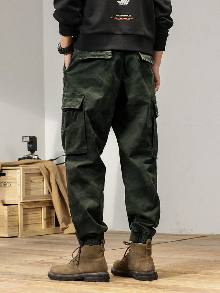 Un homme portant un pantalon cargo kaki, coupe large resserrée aux chevilles, avec des bottes brunes.