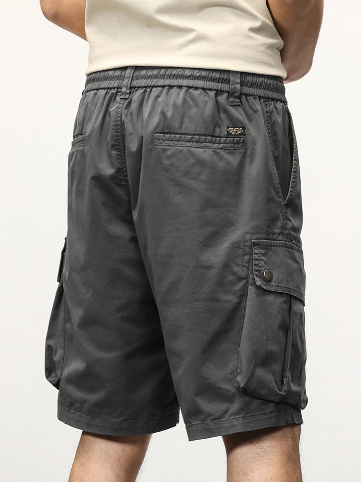 Un homme portant un short cargo gris coupe droite avec des poches latérales à boutons-pression. Tailles disponibles du 28 au 40. Fabriqué à partir de 95% coton et 5% spandex pour un confort optimal. Fermeture élastique et cordon blanc à la taille.