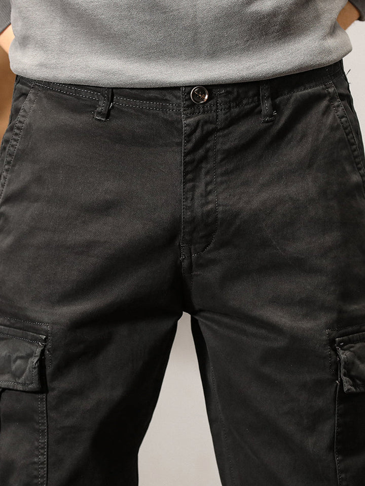 Un homme porte un pantalon cargo noir, coupe droite, avec des poches cargo sur les côtés. Fermeture par bouton et fermeture éclair. Disponible en tailles US 28 à 38. Pantalon cargo pour homme de style intemporel, confortable et polyvalent.